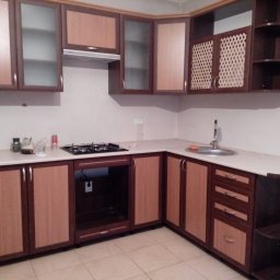 VLADEKBUD - Nowoczesna zabudowa kuchenna w odcieniach brązu i beżu, z szafkami górnymi z przeszkleniami i ażurowymi frontami, oraz blatem w jasnym kolorze.