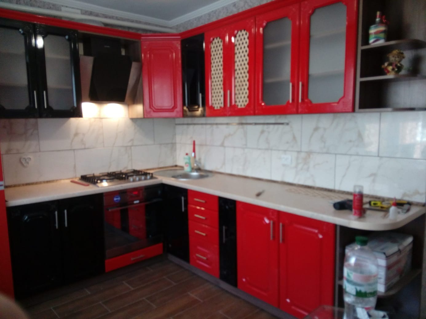Czerwono-czarna zabudowa kuchenna z błyszczącymi frontami i marmurkową glazurą. Widoczny fragment blatu z akcesoriami. Ujęcie z poziomu podłogi.