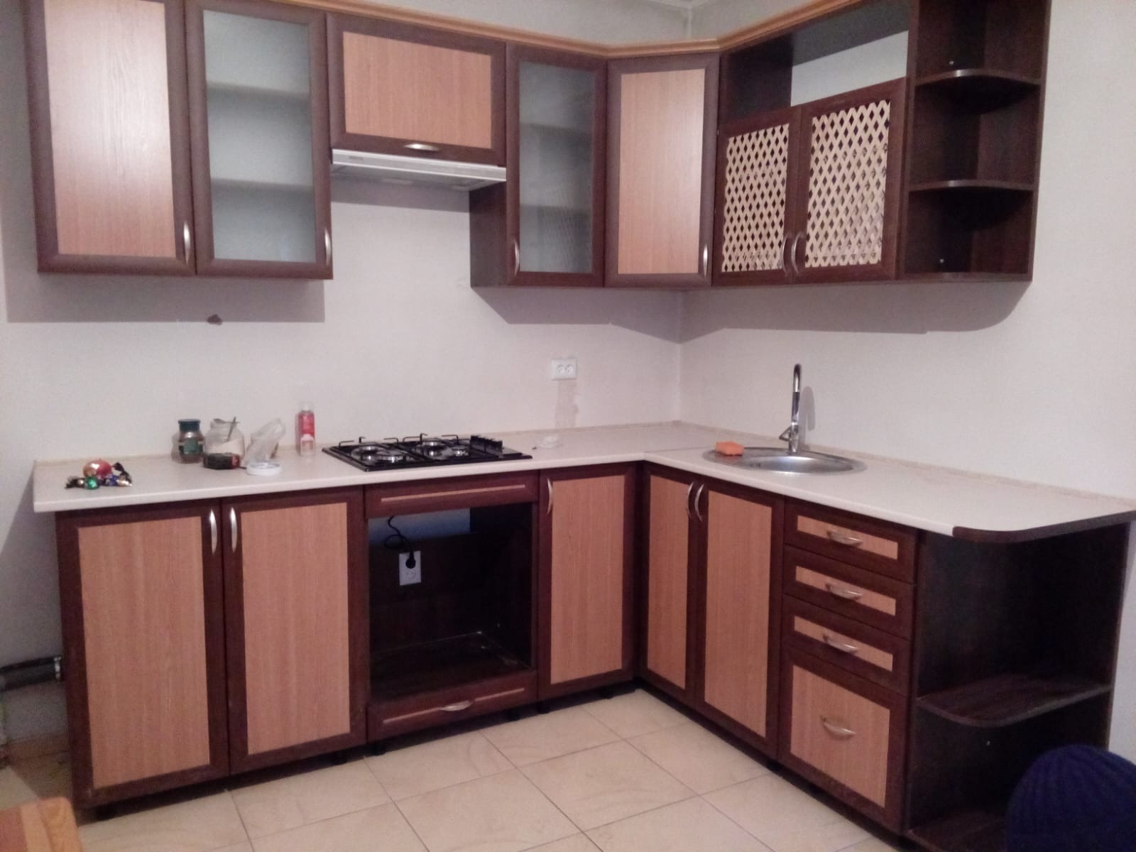 Nowoczesna zabudowa kuchenna w odcieniach brązu i beżu, z szafkami górnymi z przeszkleniami i ażurowymi frontami, oraz blatem w jasnym kolorze.