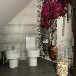 FESTGATE SPÓŁKA Z OGRANICZONĄ ODPOWIEDZIALNOŚCIĄ - Nowoczesna łazienka na poddaszu z szarą glazurą, białą armaturą (bidet i toaleta) oraz fototapetą z motywem kwiatowym i śródziemnomorskim.