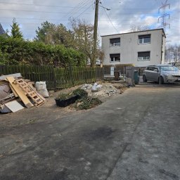 Kornel Ogrody - Teren po wycince drzew i krzewów: gałęzie w pojemniku, drewno, gruz, worki. Widoczny płot, budynek mieszkalny i zaparkowany samochód. Prace porządkowe w toku.