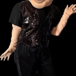 Ewelina Polus - Osoba w kostiumie z dużą głową, czarnym topem, błyszczącą kamizelką i beżowymi rękawiczkami, pozująca na czarnym tle. Nietypowy strój.