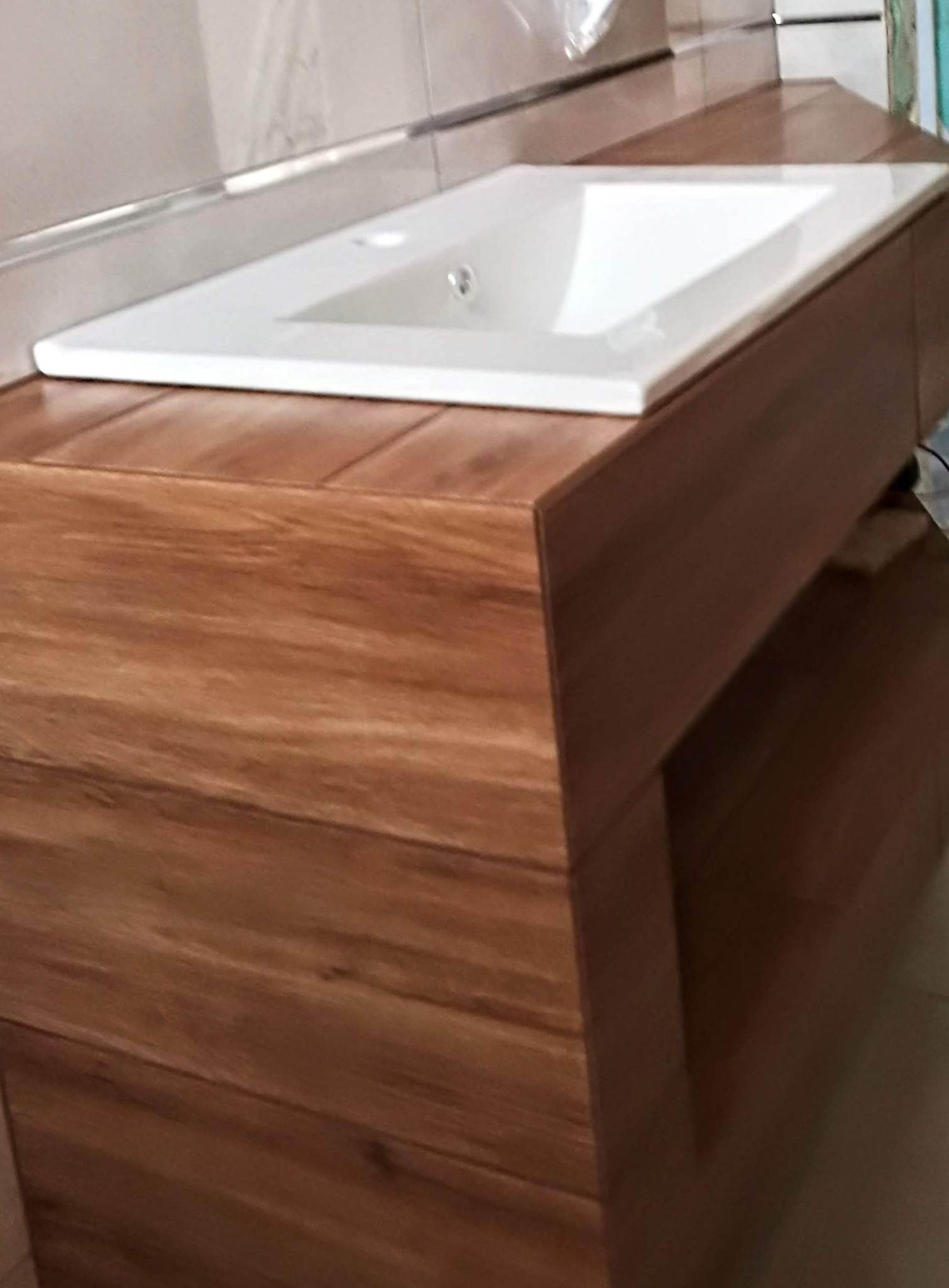 Nowoczesna umywalka nablatowa z szafką o drewnianym wykończeniu w łazience. Minimalistyczny design, jasne płytki w tle, ciepłe oświetlenie.