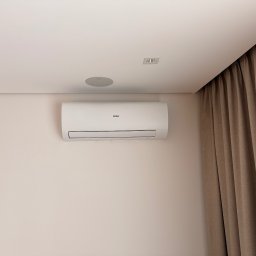 Air-Tech Piotr Dębek - Biały klimatyzator Haier na ścianie w jasnym wnętrzu, z widocznymi głośnikami sufitowymi i zasłonami w tle. Minimalistyczny design.