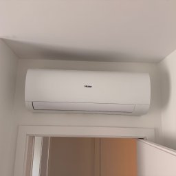 Air-Tech Piotr Dębek - Biała klimatyzacja Haier zamontowana nad drzwiami w jasnym pomieszczeniu. Widoczny fragment ściany i sufitu. Minimalistyczny design urządzenia.