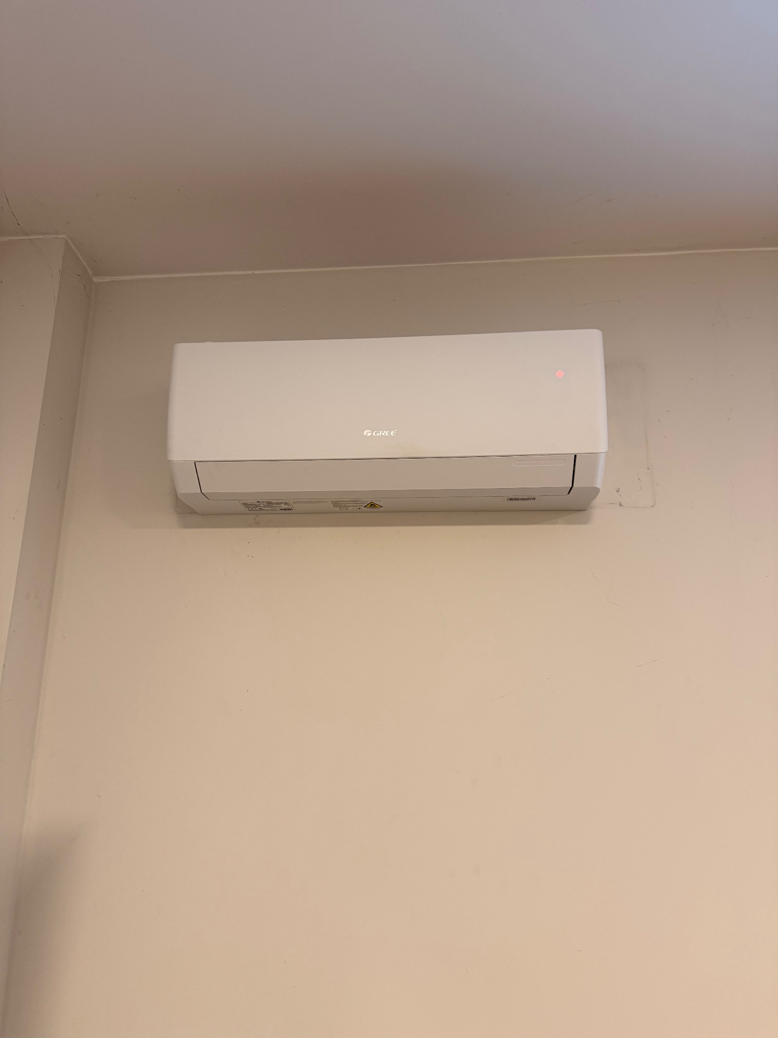 Biała klimatyzacja marki Gree zamontowana na beżowej ścianie. Widoczny wskaźnik LED. Minimalistyczny design.