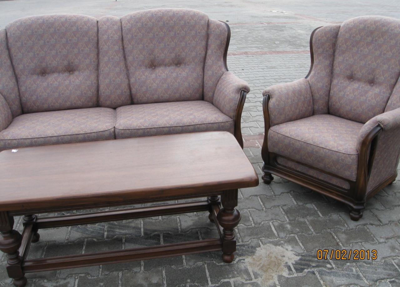 Stylowy komplet wypoczynkowy: sofa dwuosobowa i fotel uszak z tapicerką w geometryczny wzór, uzupełnione stolikiem kawowym na toczonych nogach, ustawione na szarej kostce brukowej.