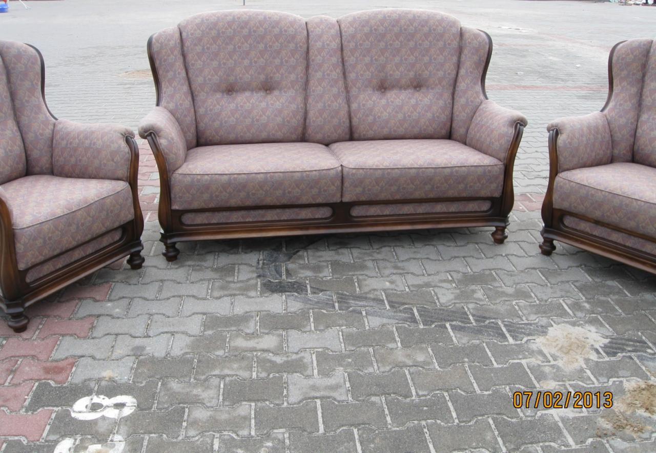 Stylowy komplet wypoczynkowy: dwuosobowa sofa i dwa fotele z brązowym drewnianym wykończeniem i tapicerką w geometryczny wzór, ustawiony na szarej kostce brukowej.