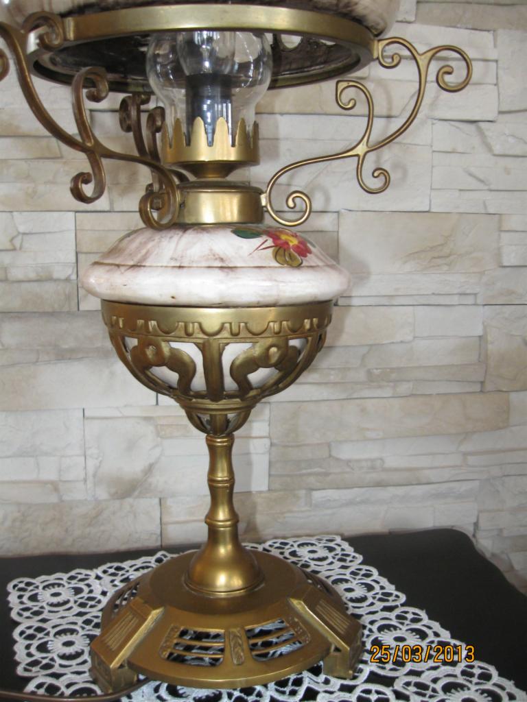 Antyczna lampa stołowa z porcelanową bazą zdobioną kwiatowym motywem i mosiężną konstrukcją, stojąca na koronkowej serwetce.