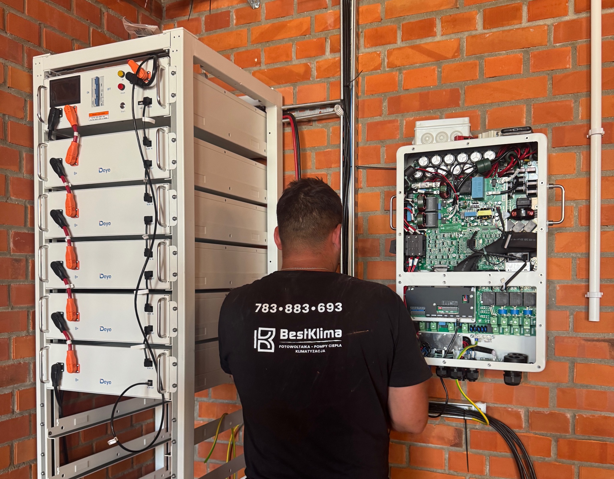 Instalacja magazynu energii Deye i falownika na ceglanej ścianie przez technika BestKlima. Widoczne kable i podłączenia. Specyficzny montaż na szynie.
