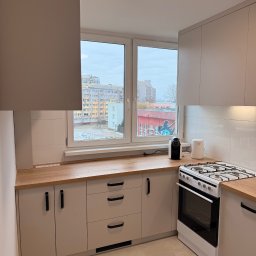 sebastian schönwetter - Jasna kuchnia z drewnianym blatem, widokiem na blok zza okna i nowoczesnym oświetleniem sufitowym. Minimalistyczny design, sprzęt AGD na blacie.