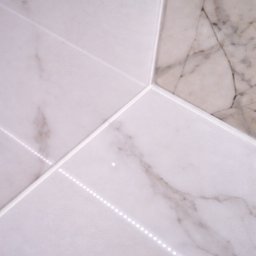 Robota na Glanc - Białe i beżowe marmurowe płytki ułożone pod kątem, z widoczną listwą LED wzdłuż spoin. Detal wykończenia podłogi lub ściany.