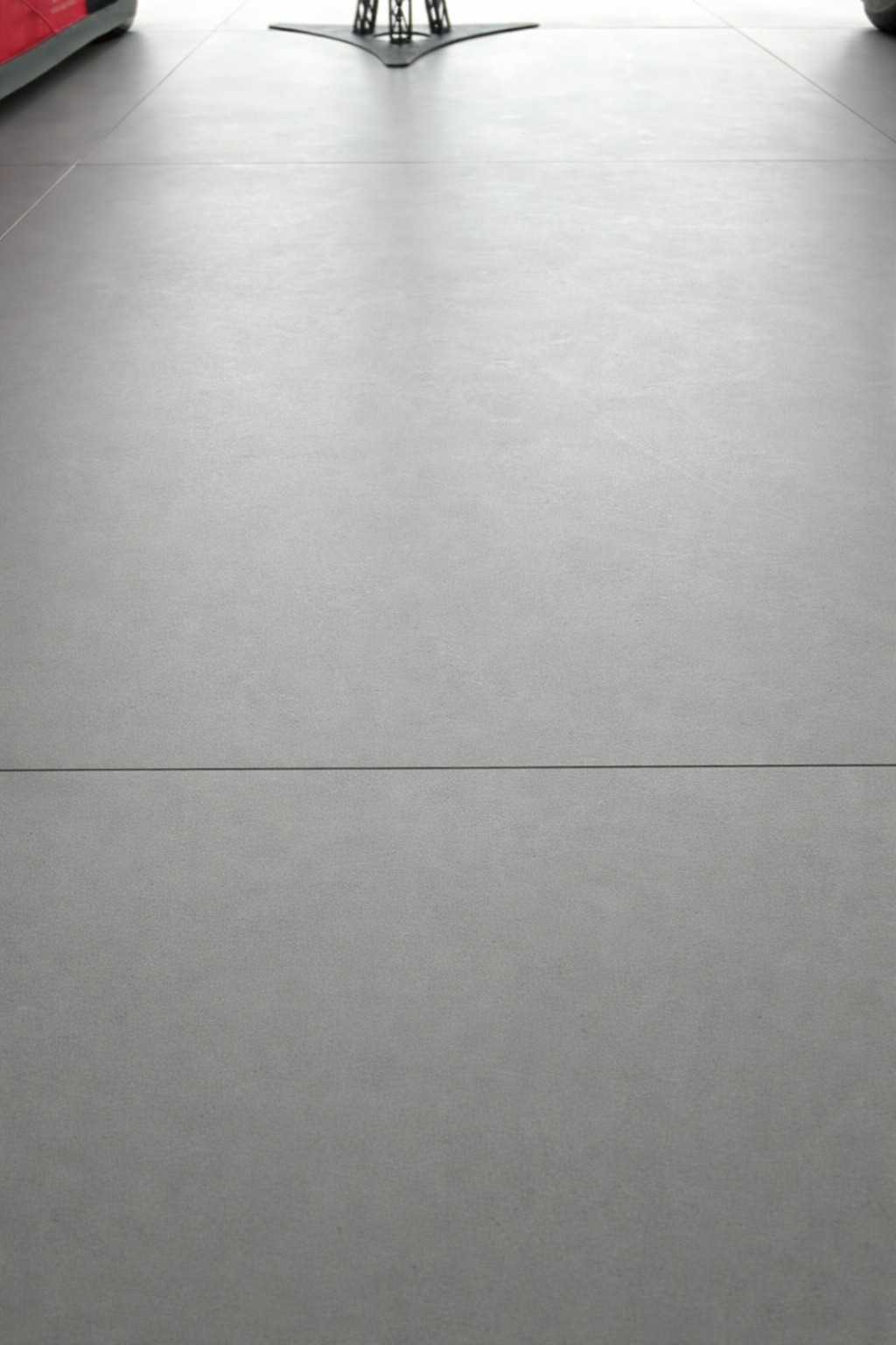 Szara, matowa podłoga z płytek po czyszczeniu, widoczna z bliska, z elementami wyposażenia w tle. Minimalistyczny design i czyste linie.