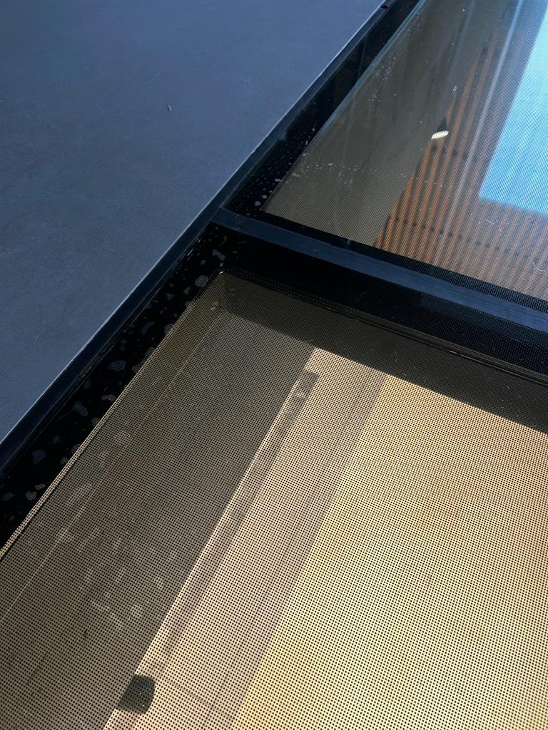 Szczegółowe ujęcie brudnej szyby okiennej z widocznymi smugami i zaciekami, kontrastujące z czystą powierzchnią obok. Widoczne drobne zabrudzenia na ramie okiennej.