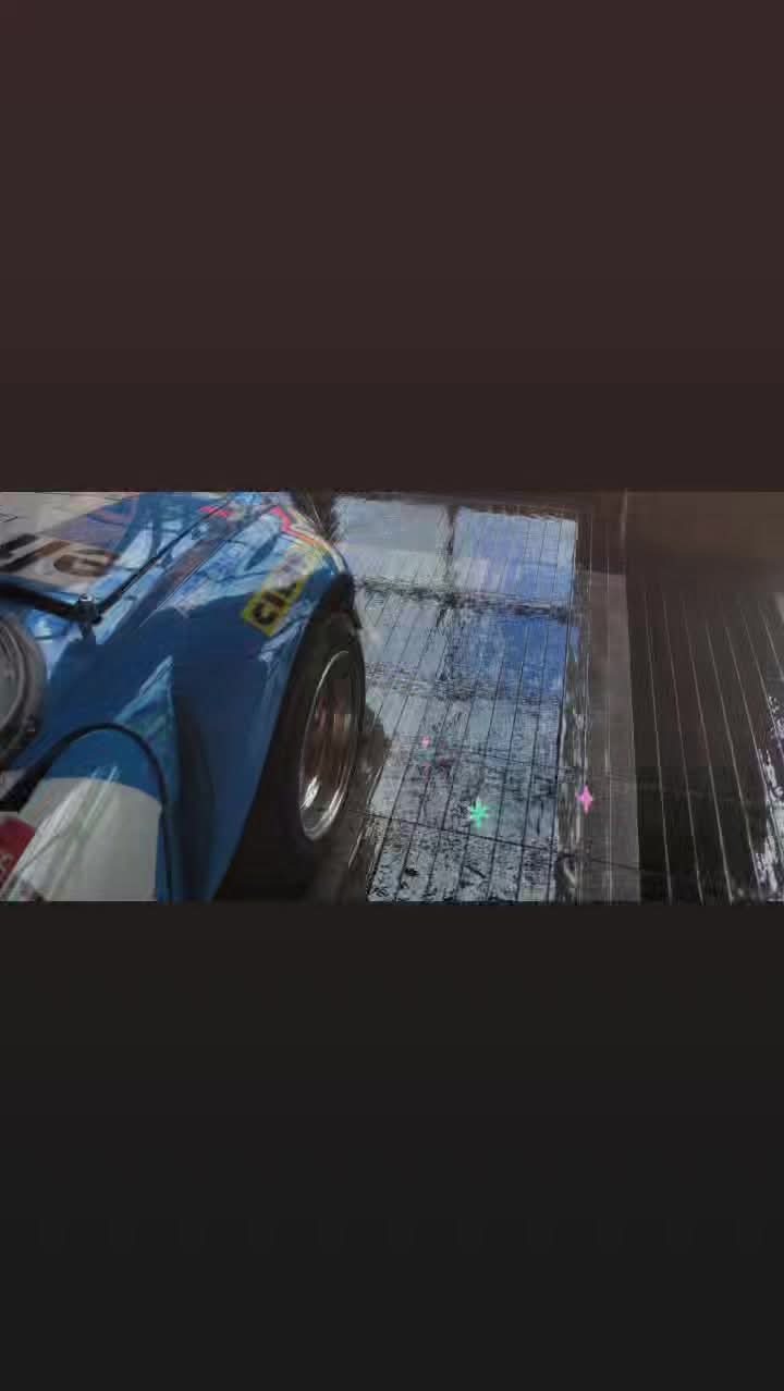 Błyszczący, niebieski samochód wyścigowy po umyciu, z widocznymi kroplami wody na karoserii i mokrej, wyczyszczonej podłodze w myjni.