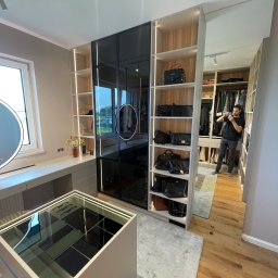 FURNIGO - Nowoczesna garderoba na wymiar z czarnymi, szklanymi frontami i oświetleniem LED. Widoczny mężczyzna robiący zdjęcie wnętrza. Na półkach torebki.