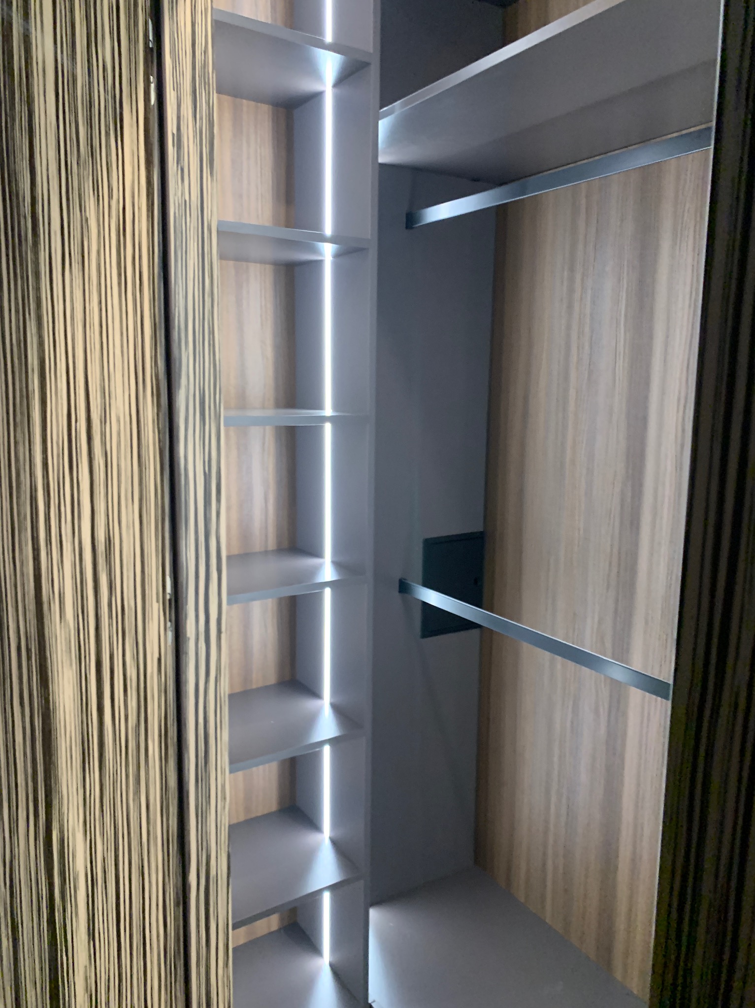 Wnętrze szafy na wymiar z oświetleniem LED, półkami i drążkami na ubrania. Fronty szafy w kolorze drewna z wyraźnym rysunkiem słojów.