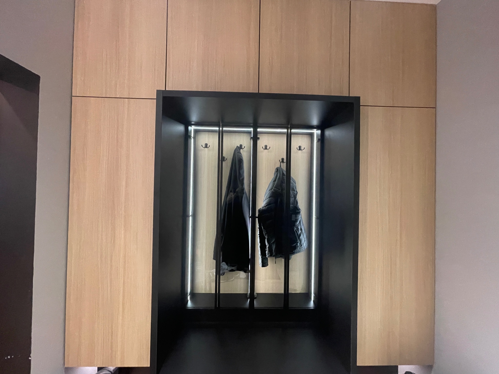 Nowoczesna szafa wnękowa z oświetleniem LED i wieszakami na ubrania. Jasne drewno i czarne elementy tworzą elegancki kontrast.