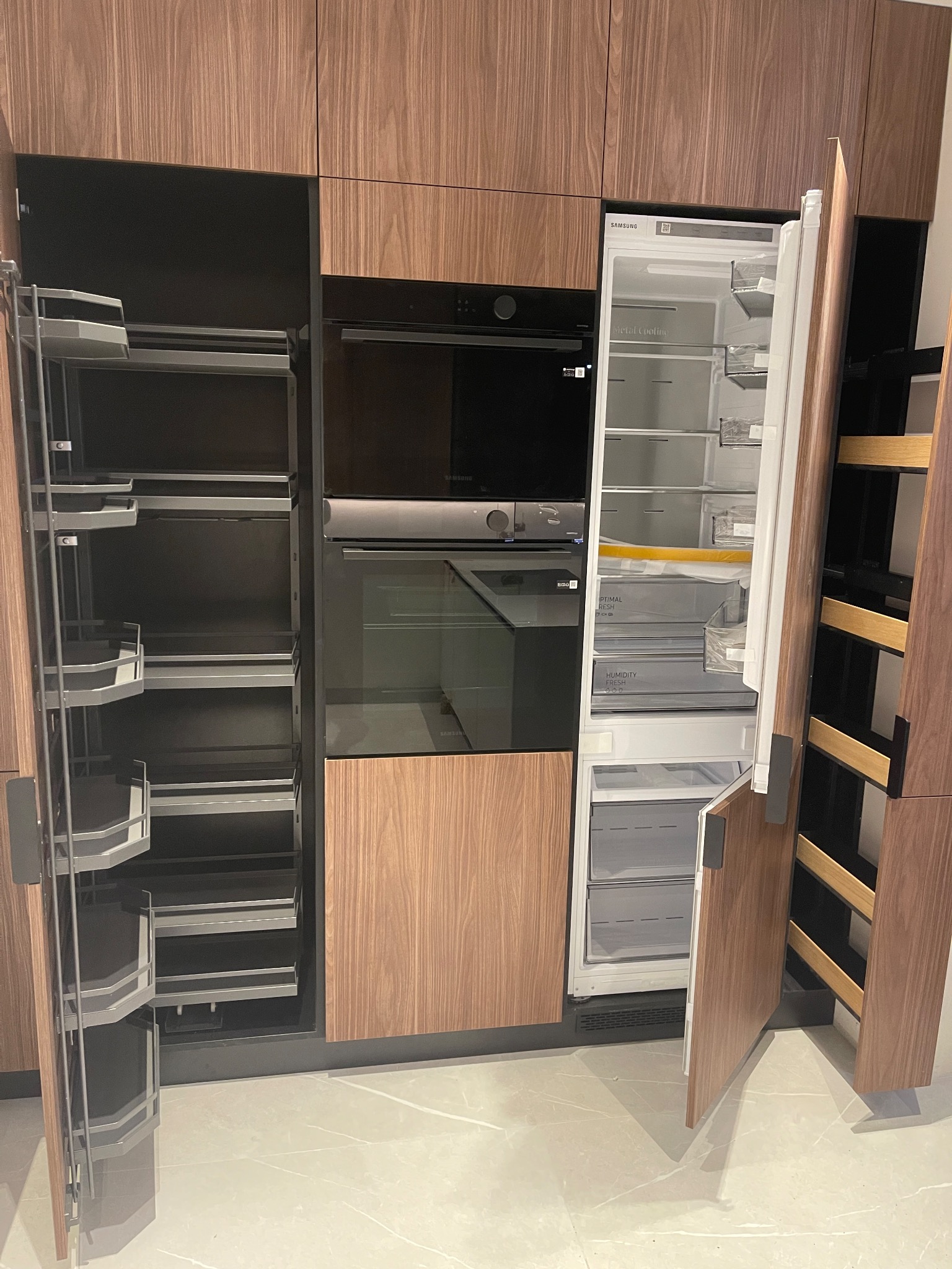 Nowoczesna kuchnia z drewnianymi frontami: zabudowa z piekarnikiem, lodówką i wysuwanymi półkami cargo. Minimalistyczny design, jasna podłoga.