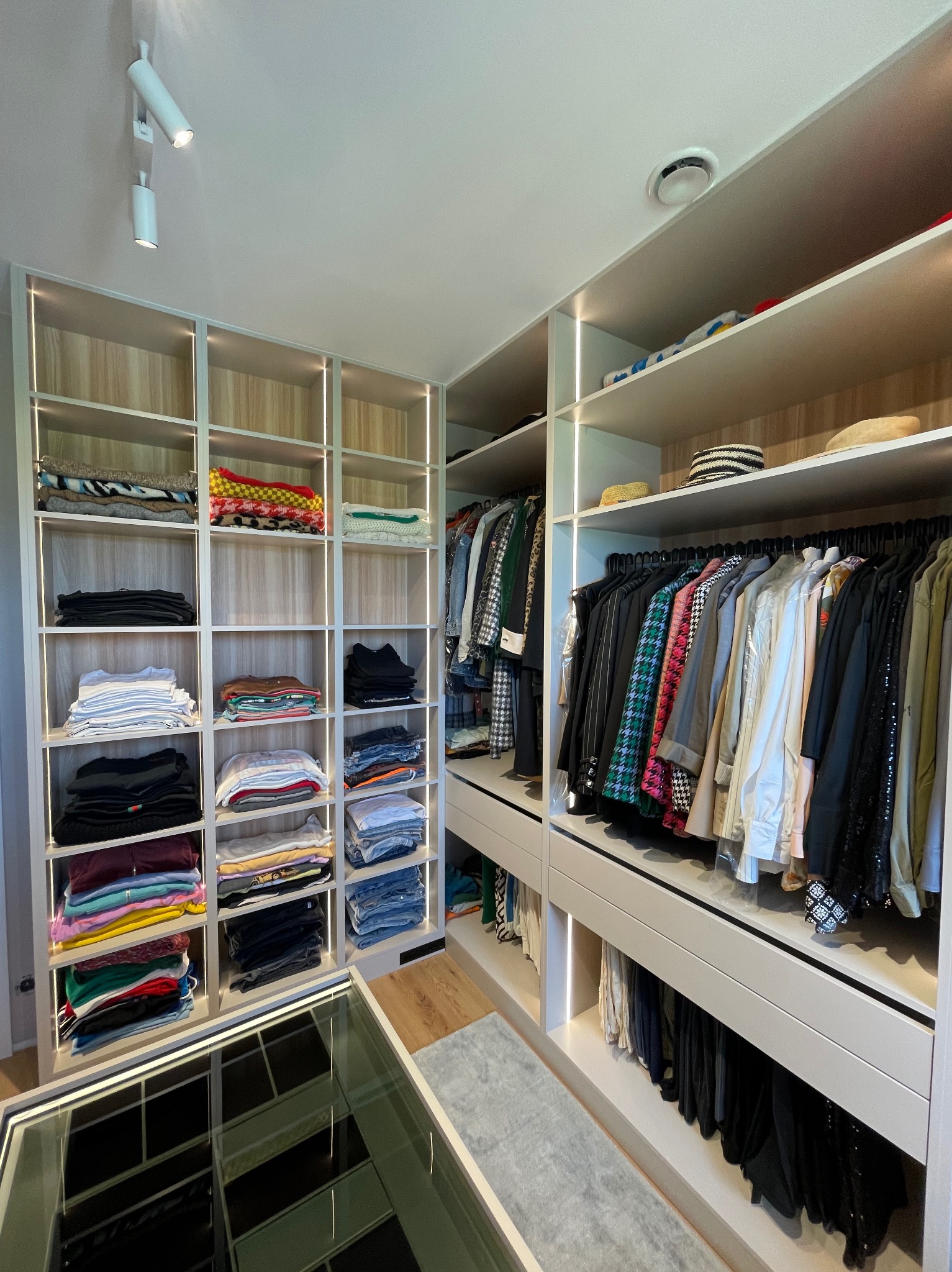 Nowoczesna garderoba na wymiar z oświetleniem LED. Jasne półki z ubraniami, wieszaki z odzieżą. Minimalistyczny design, funkcjonalne rozwiązanie do przechowywania.