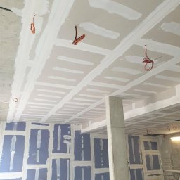 DARBUD Dariusz Baran - Sufit i ściany z płyt gipsowo-kartonowych, przygotowane do dalszych prac wykończeniowych, widoczne kable elektryczne i szpachlowane łączenia.