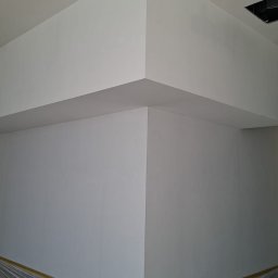 Kameleon Studio - Wnętrze po remoncie: gładkie, białe ściany i sufit z żółtymi punktami świetlnymi. Podłoga zabezpieczona folią malarską z taśmą. Widok na narożnik pomieszczenia.