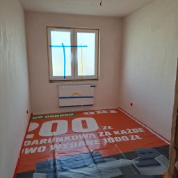 Kameleon Studio - Pokój po szpachlowaniu ścian, zabezpieczony folią ochronną na podłodze i oknach. Widoczne gładkie, jasne ściany przygotowane do malowania. Etap prac wykończeniowych.