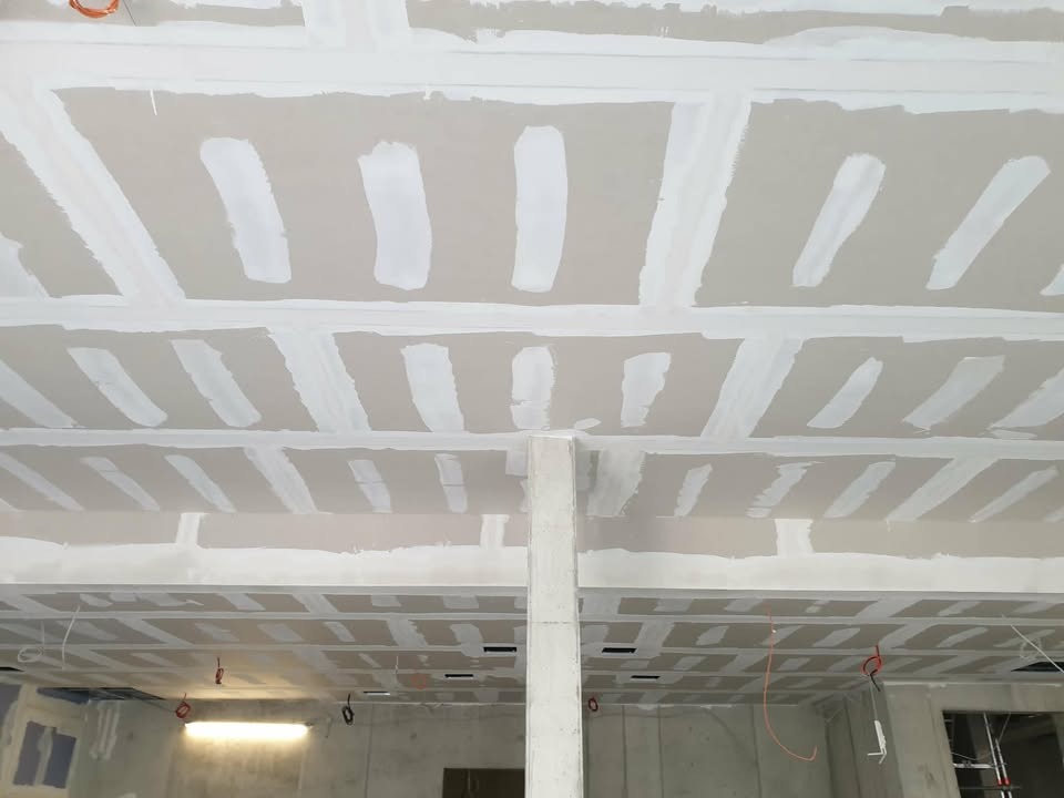 Sufit z płyt gipsowo-kartonowych, wstępnie wyszpachlowany, z widocznymi łączeniami i miejscami po wkrętach, przygotowany do dalszych prac wykończeniowych.