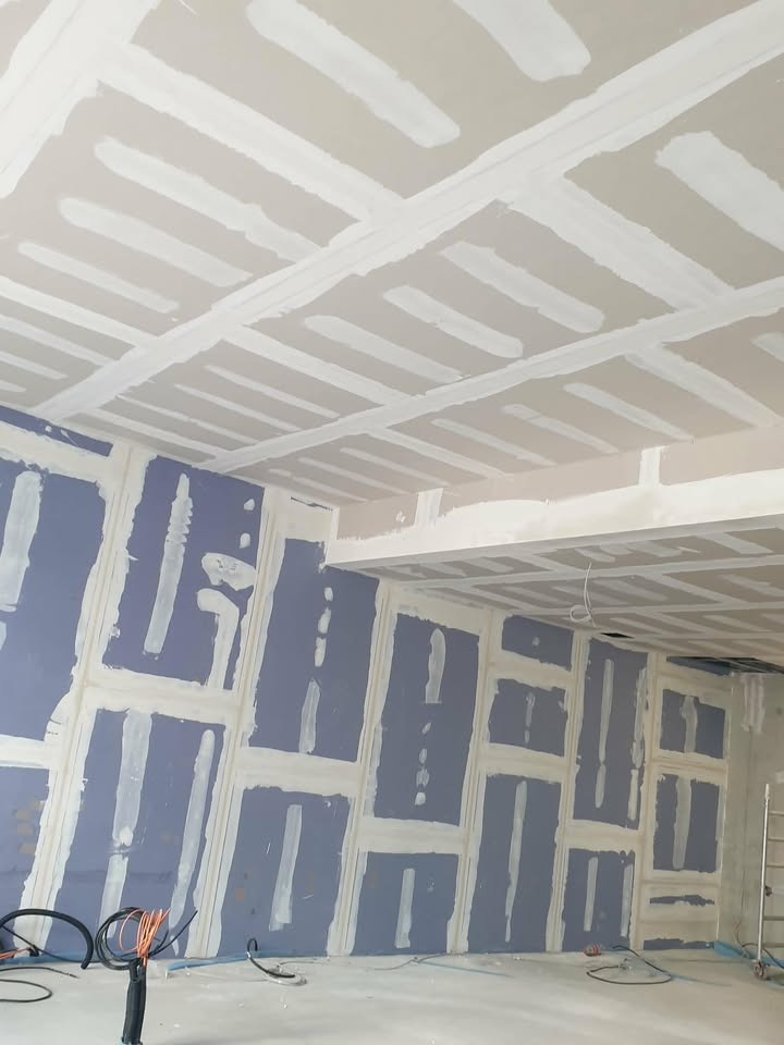 Ściana i sufit z płyt gipsowo-kartonowych, przygotowane do szpachlowania. Widoczne łączenia płyt wypełnione masą szpachlową. W tle drabina i przewody.
