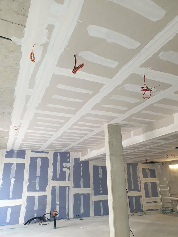 Sufit i ściany z płyt gipsowo-kartonowych, przygotowane do dalszych prac wykończeniowych, widoczne kable elektryczne i szpachlowane łączenia.