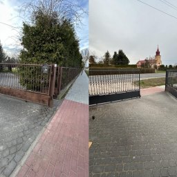 Alan Urban - Porównanie: Stara, rdzawa brama z metaloplastyki kontra nowa, czarna brama z metaloplastyki. Kostka brukowa w dwóch odcieniach szarości. Widok na ulicę i kościół w tle.