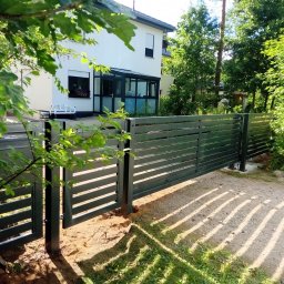 JK STAHL BAU - Nowoczesna, pozioma brama wjazdowa z metalowymi przęsłami, częściowo otwarta, na tle białego domu i zieleni. Widoczne ślady montażu w ziemi.