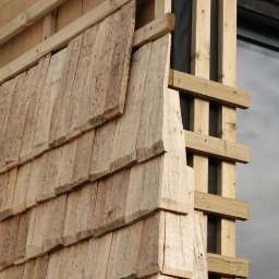 Grzegorz Prokopowicz DOMGUSTO - Fragment elewacji z drewnianym szalunkiem, widoczne elementy konstrukcyjne i okno. Detal montażu drewnianej okładziny elewacyjnej na budynku.