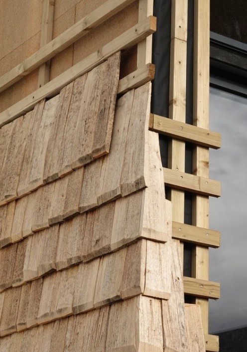 Fragment elewacji z drewnianym szalunkiem, widoczne elementy konstrukcyjne i okno. Detal montażu drewnianej okładziny elewacyjnej na budynku.