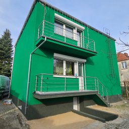 Was&Bud - Jaskrawo zielony budynek z balkonami i nierdzewną balustradą, po renowacji elewacji. Widoczne detale wykończenia i drabina na ścianie. Ujęcie z dołu.