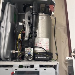 Install-Tech - Otwarty piec gazowy marki Buderus z widocznymi elementami instalacji, przewodami i wyświetlaczem wskazującym temperaturę 37.4°C. Widoczne komponenty ebmpapst i Honeywell.