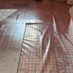 Install-Tech - Układanie folii aluminiowej i maty grzewczej z siatką w pomarańczową kratę na podłodze, przygotowanie do montażu ogrzewania podłogowego. Widok z góry.
