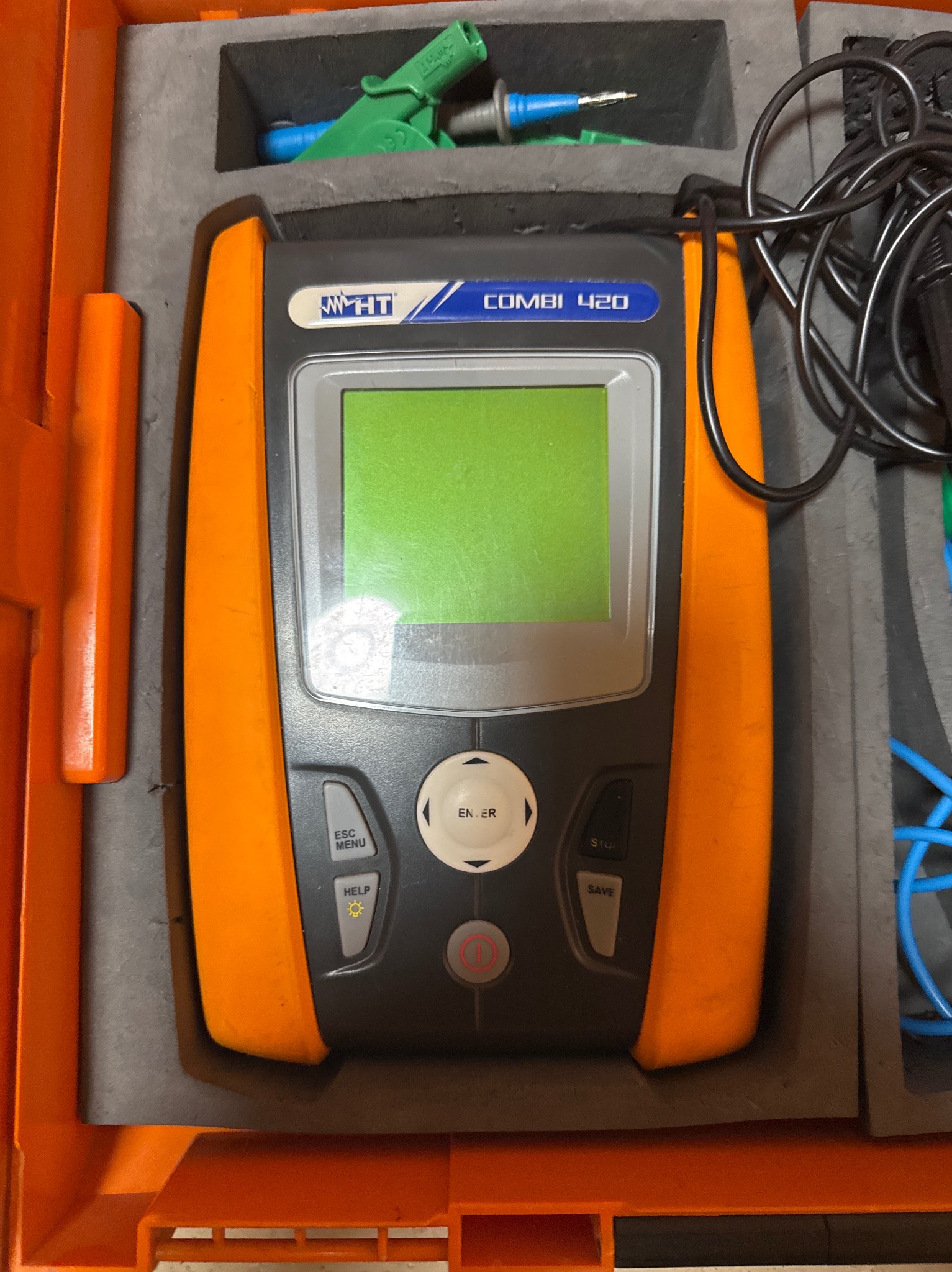 Miernik wielofunkcyjny HT Combi 420 w pomarańczowej obudowie, z przewodami i akcesoriami, umieszczony w szarej, wyściełanej skrzynce transportowej.