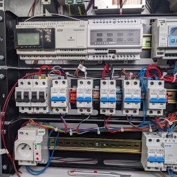 ELEKTROMECHANIKA Dominik Sobczyński - Rozdzielnica elektryczna z zabezpieczeniami, sterownikami i okablowaniem w metalowej obudowie. Widoczne bezpieczniki Schrack, sterowniki F&F i Satel.