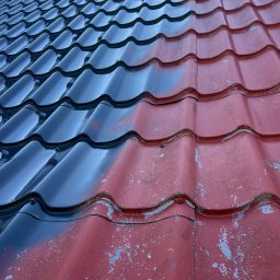 MALVERTO SP. Z O. O. - Częściowo pomalowany dach z blachodachówki w kolorze czerwonym i czarnym. Widoczne ślady starej farby. Ujęcie z dołu, ukazujące strukturę i detale pokrycia.