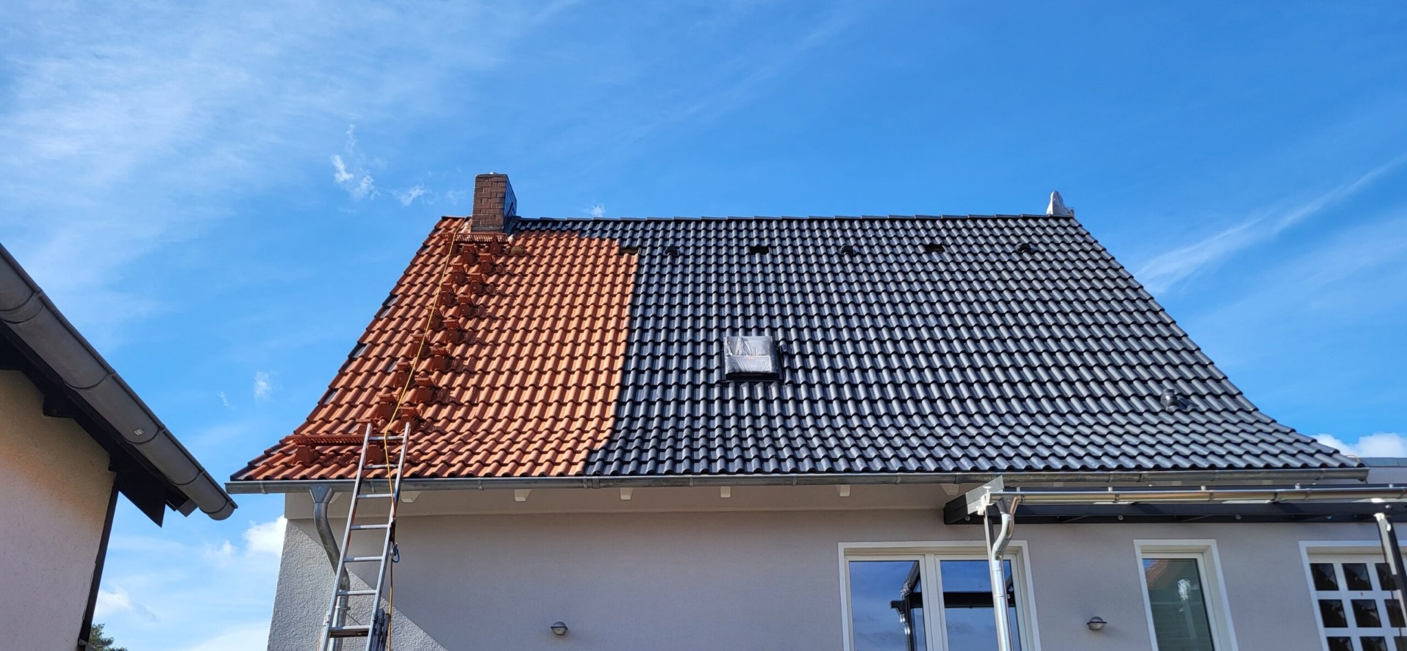 Dachówka ceramiczna po części pomalowana na grafitowo, druga część w kolorze ceglastym. Widoczna drabina oparta o budynek. Błękitne niebo.