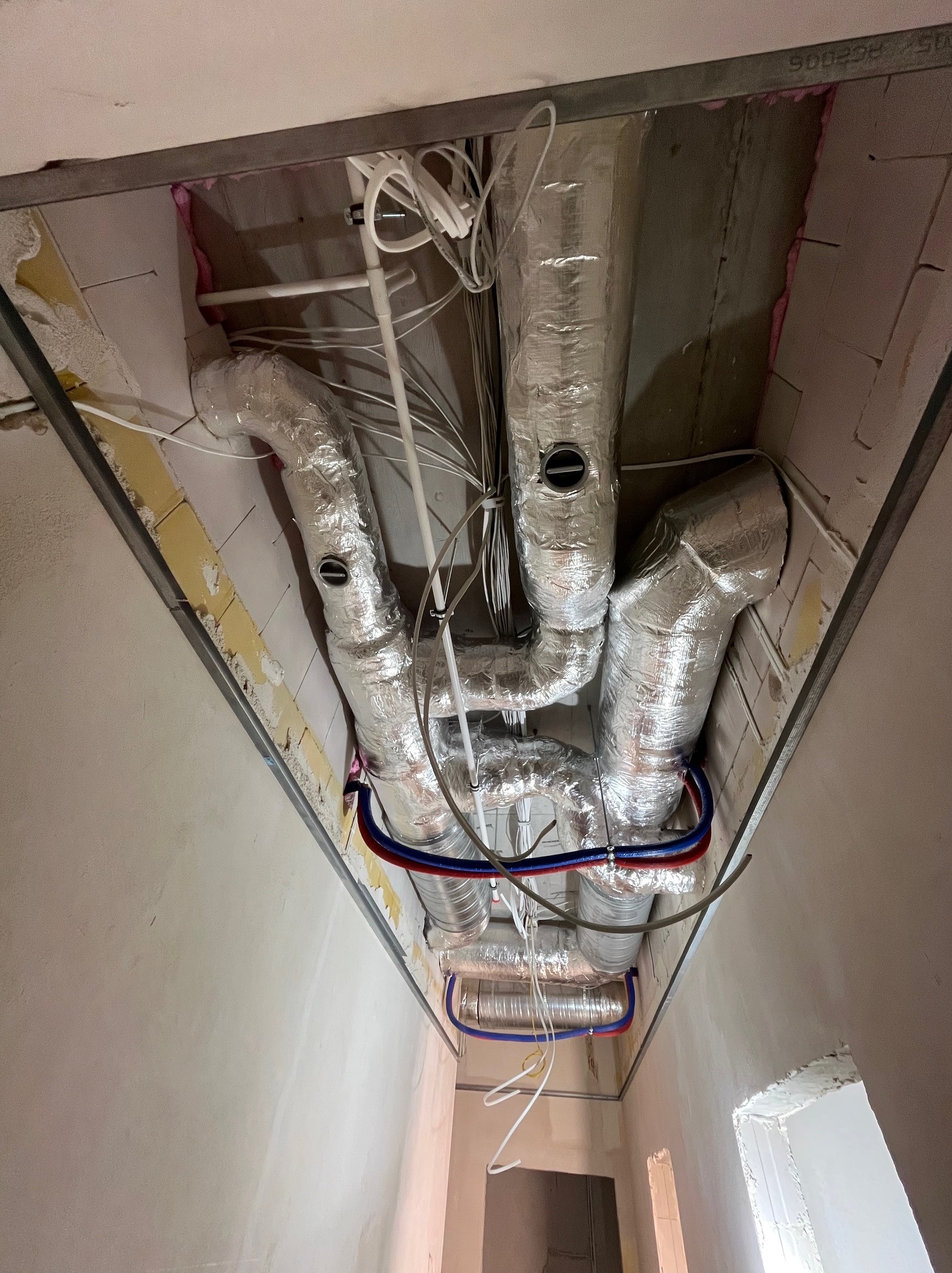 Skomplikowany system wentylacyjny z rurami w izolacji aluminiowej, widoczny pod sufitem w trakcie montażu. Instalacja prowadzona w przestrzeni między stropem a sufitem podwieszanym.