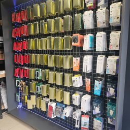 Centrum Serwisowe - Ekspozycja akcesoriów GSM: szkła hartowane, ładowarki, kable USB i słuchawki. Różnorodność produktów na metalowej siatce z podświetleniem LED.