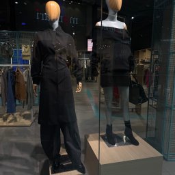 Dominik Kowalczyk - Dwa manekiny w czarnych stylizacjach w witrynie sklepowej. Jeden w płaszczu, drugi w sukience z odkrytymi ramionami i torebką. Minimalistyczny design i nowoczesny wystrój.