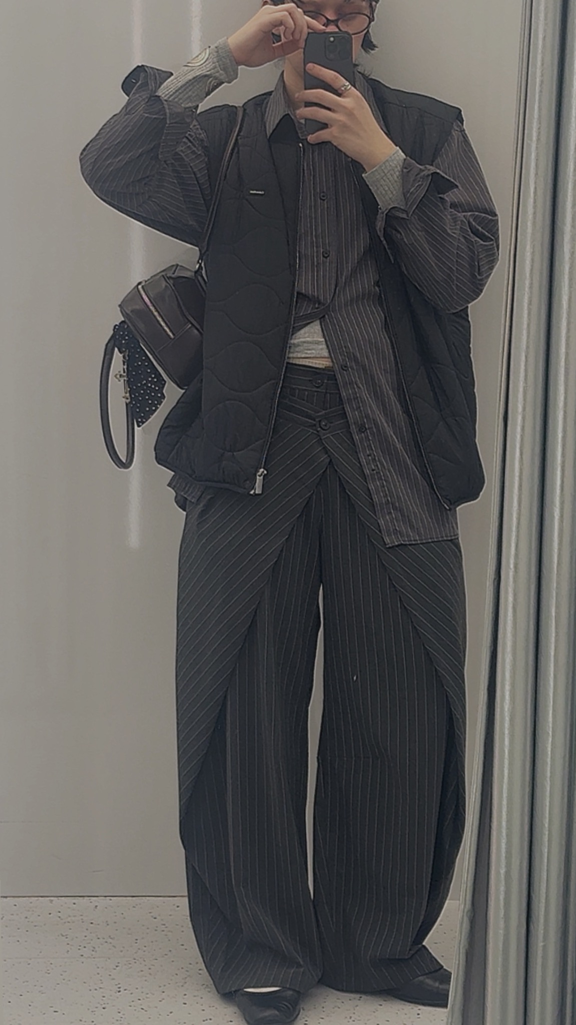 Osoba w paski ubrana w awangardowe spodnie i kamizelkę robi selfie w lustrze, prezentując unikalny styl ubioru i modną stylizację.