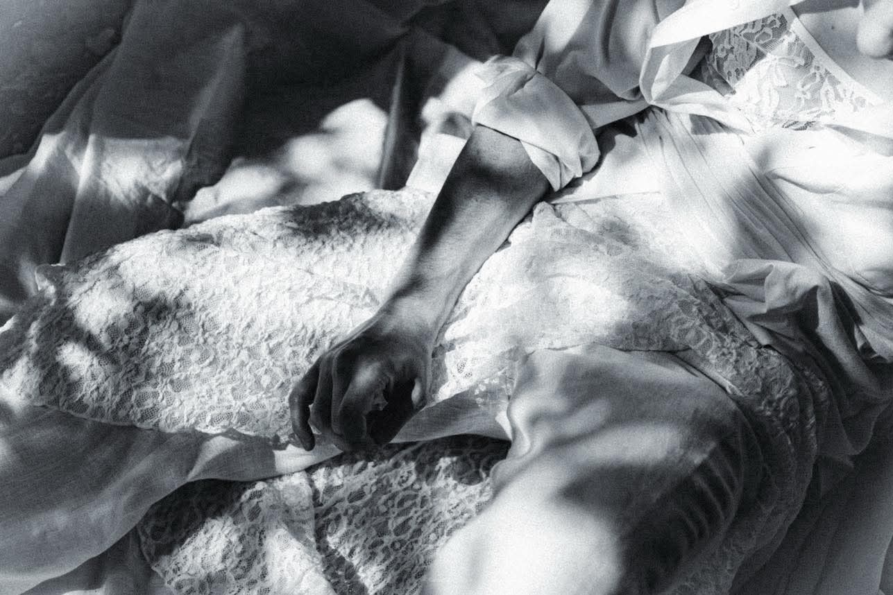 Czarno-białe zdjęcie dłoni spoczywającej na koronkowej tkaninie, z delikatnym światłem i cieniem, tworzące subtelny, artystyczny obraz.