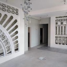 SolidHouse - Jasne wnętrze z dekoracyjnymi, białymi panelami ściennymi o ażurowych wzorach, surowy beton w tle, nowoczesna lampa wisząca i fragment rusztowania.
