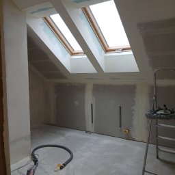 Luk bud - Poddasze w trakcie szpachlowania z oknami dachowymi, widoczne narzędzia i drabina. Ściany przygotowane pod malowanie, surowy beton na podłodze.