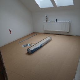 Luk bud - Podkład pod panele ułożony w pokoju na poddaszu z oknami dachowymi. Widoczna paczka paneli, listwa przypodłogowa i grzejnik. Przygotowanie do montażu podłogi.