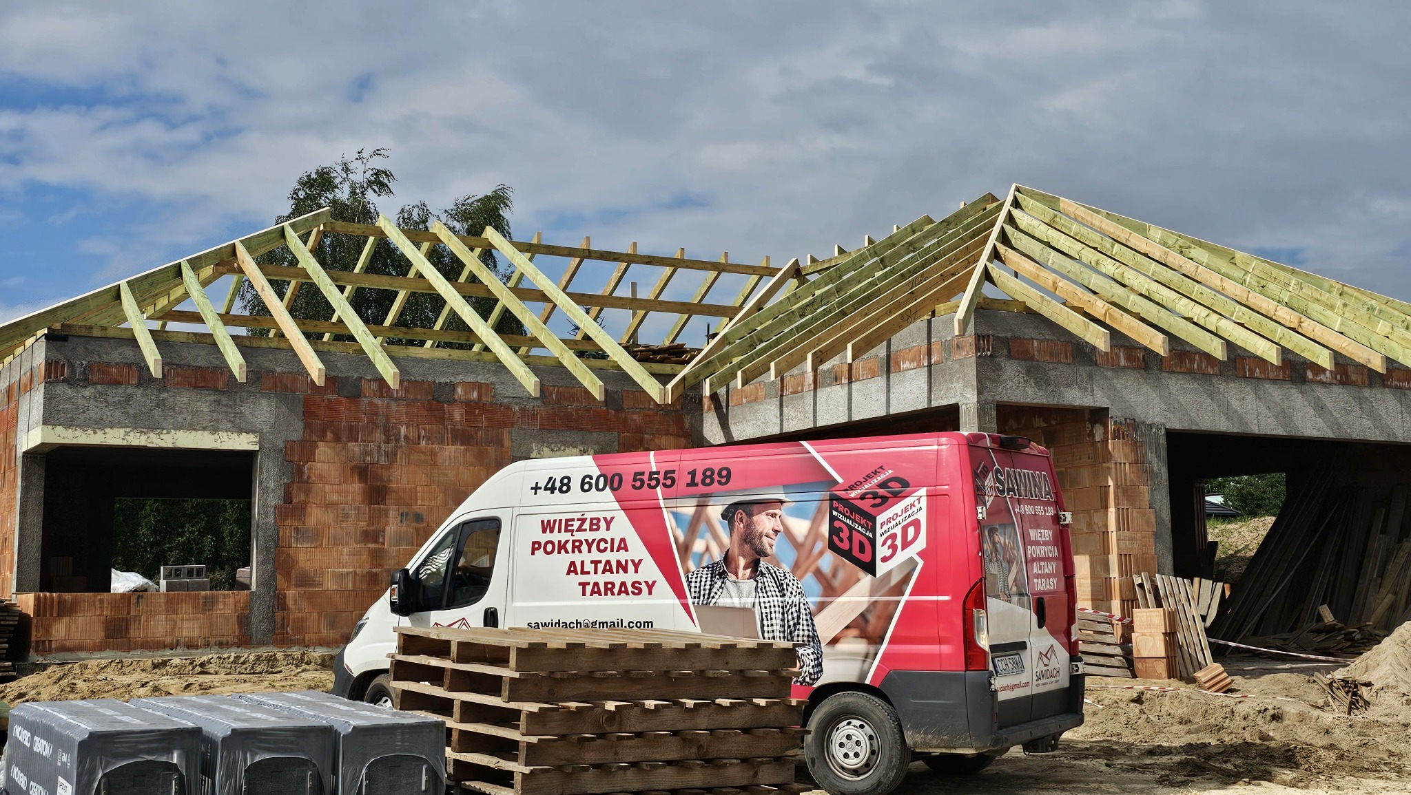 Wznoszony budynek z widoczną więźbą dachową, na pierwszym planie samochód dostawczy z reklamą firmy budowlanej. Widoczne materiały budowlane.